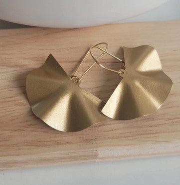 Boucles d’oreilles dorées en forme de feuille, posées sur une planche en bois.