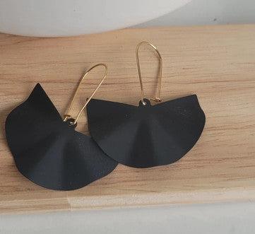 Boucles d’oreilles noires fantaisie en forme de fleur, crochet doré, posées sur bois.