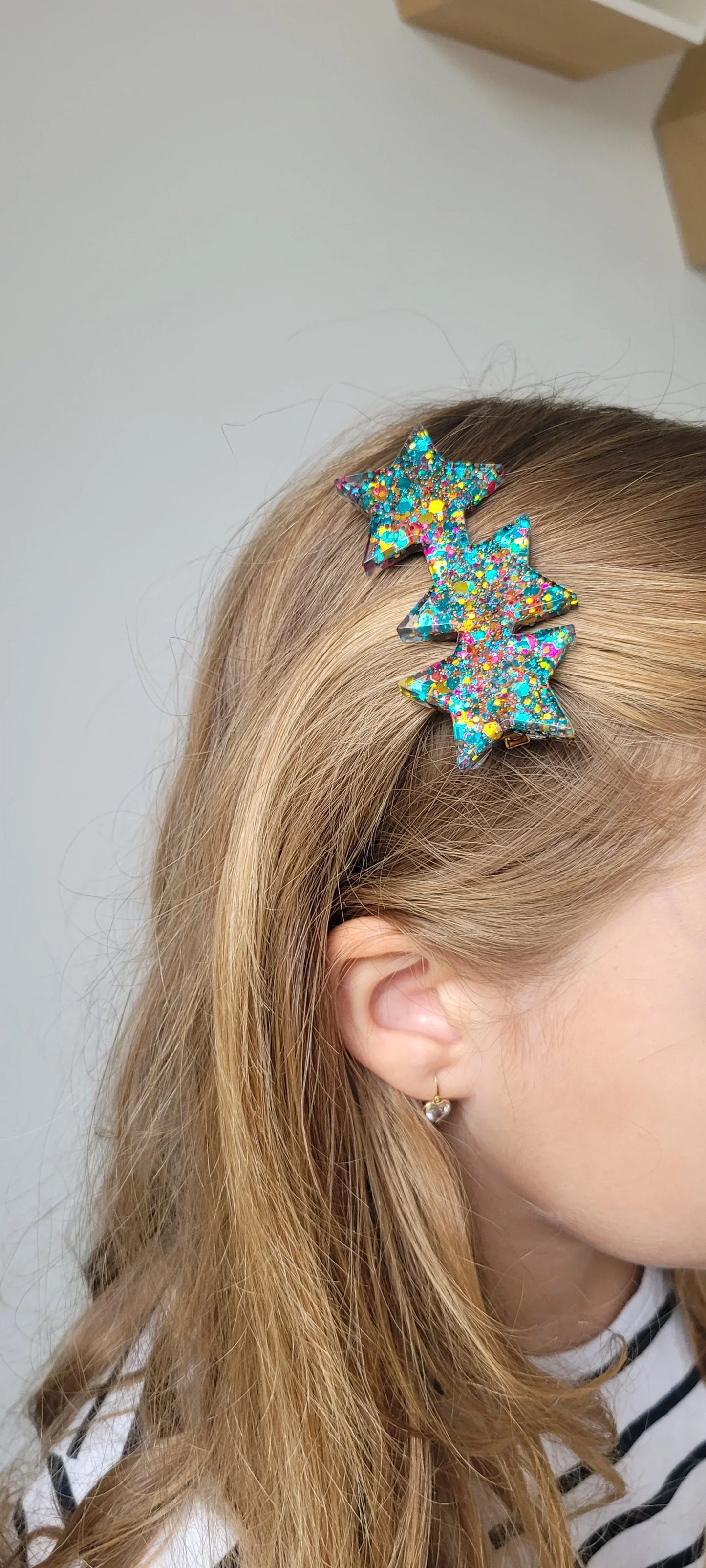 Barrette étoiles multicolores pailletées en résine sur cheveux blonds, bijou fantaisie tendance.